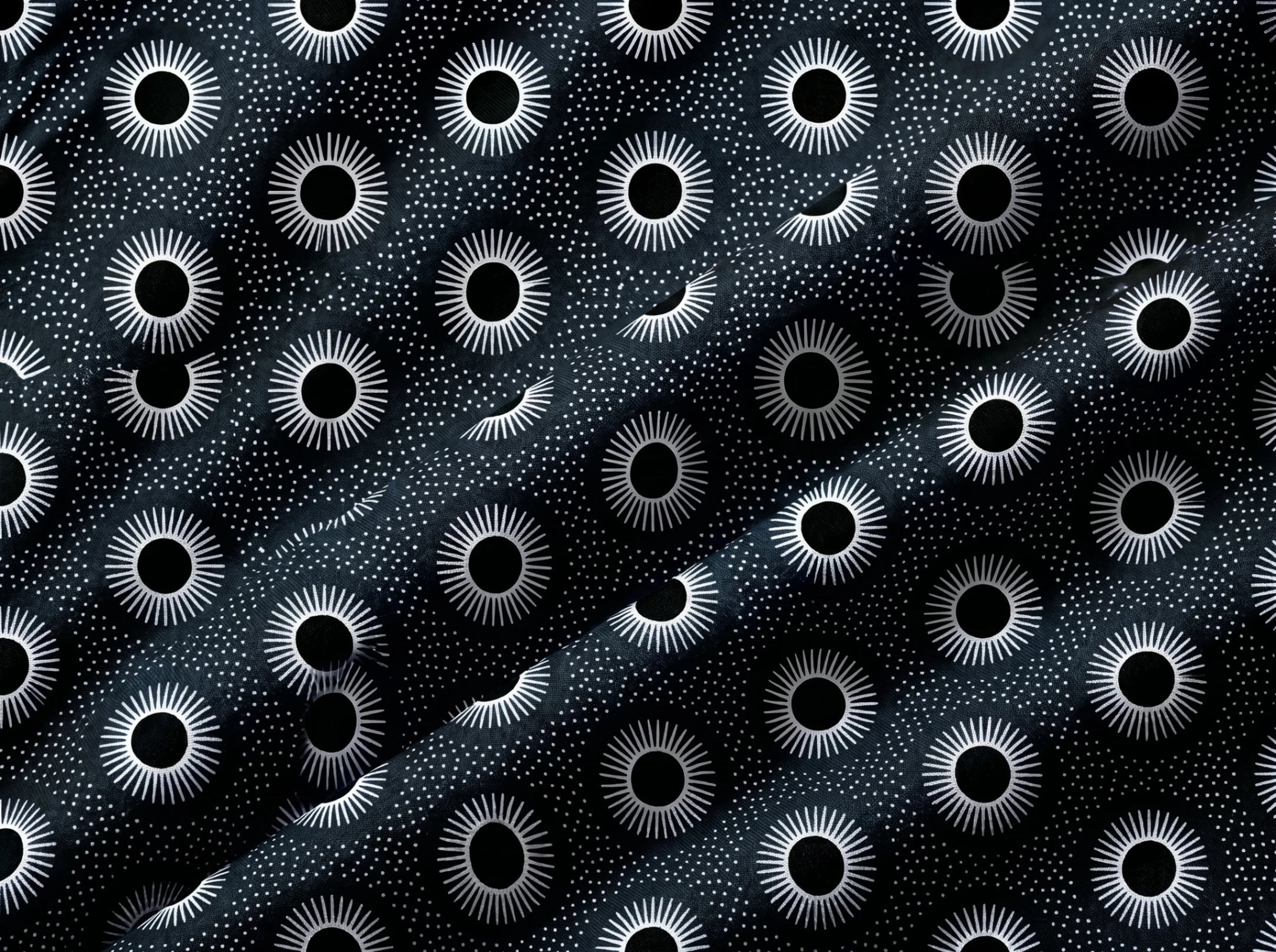 Black and white fabric featuring a repeating pattern of stylized sunburst eyes and small stars, with a diagonal satin-like sheen.
